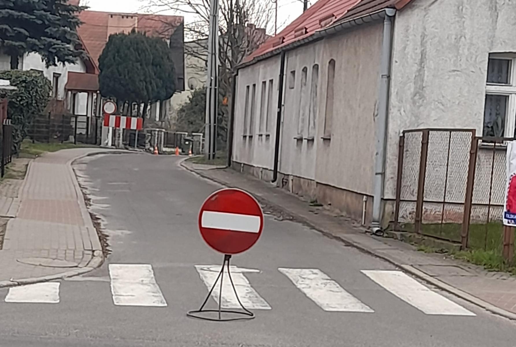 Znak okrągły czerowny z paskiem białym, zakaz wjazdu ustawiony na drodze, w oddali kolejny znak i barierka biało-czerowna 