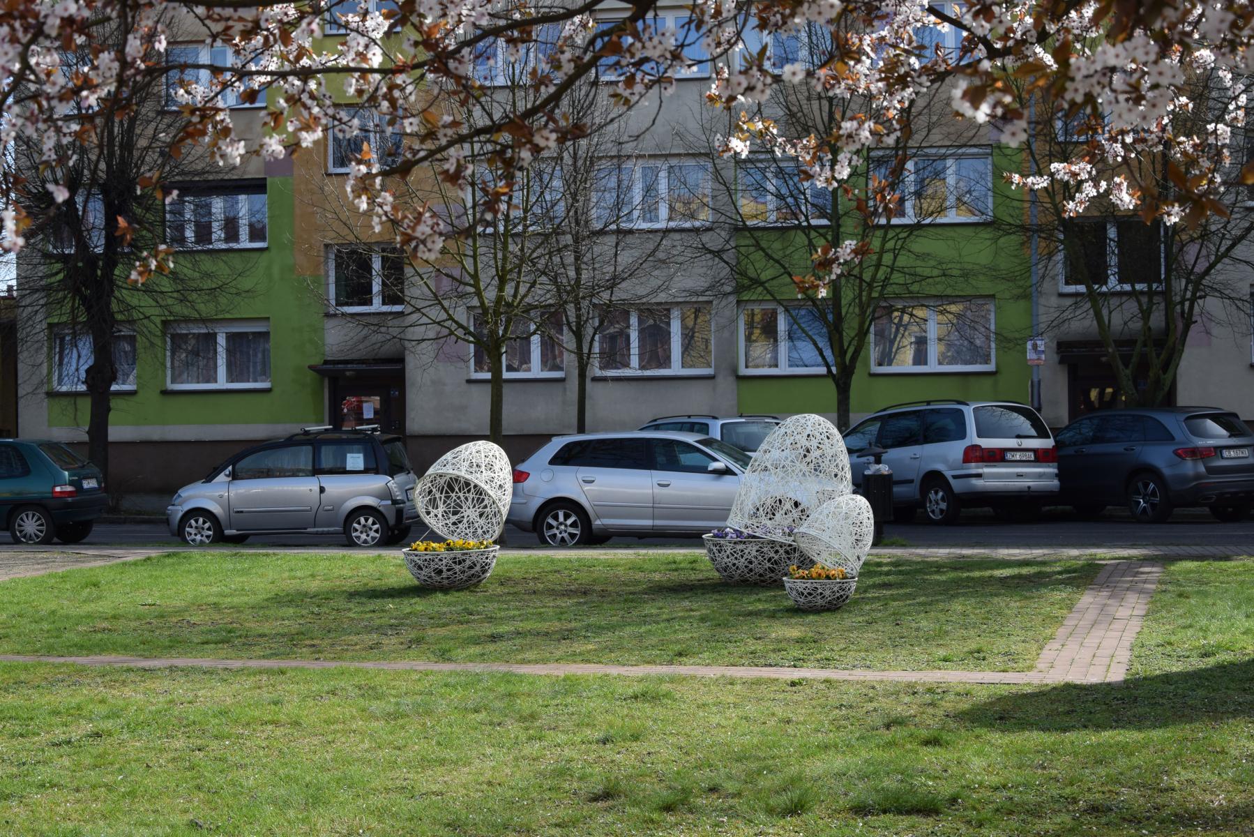 Trzykonstrukcje ażurowe jajek, w których posadzone są bratki. Teren zielony