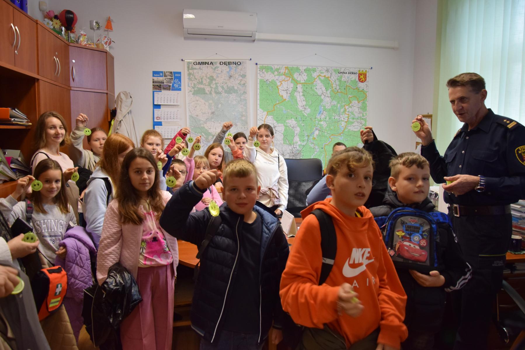 Dzieci w biurze komendanta Straży Miejskiej. W rękach trzymają odblaski. W tle na ścianach mapa  