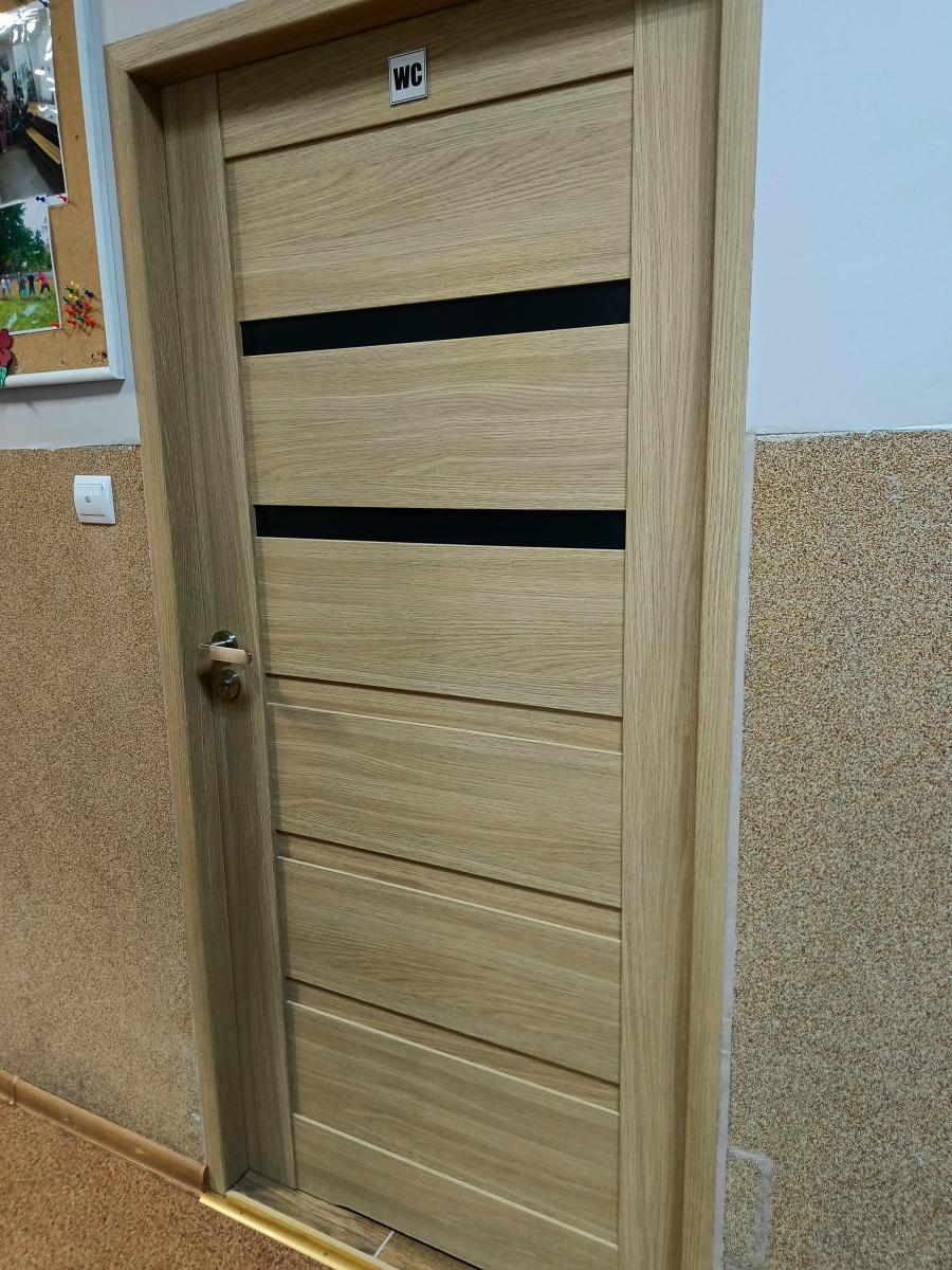 Drzwi wejściowe jasne drewno, na górze naklejka WC