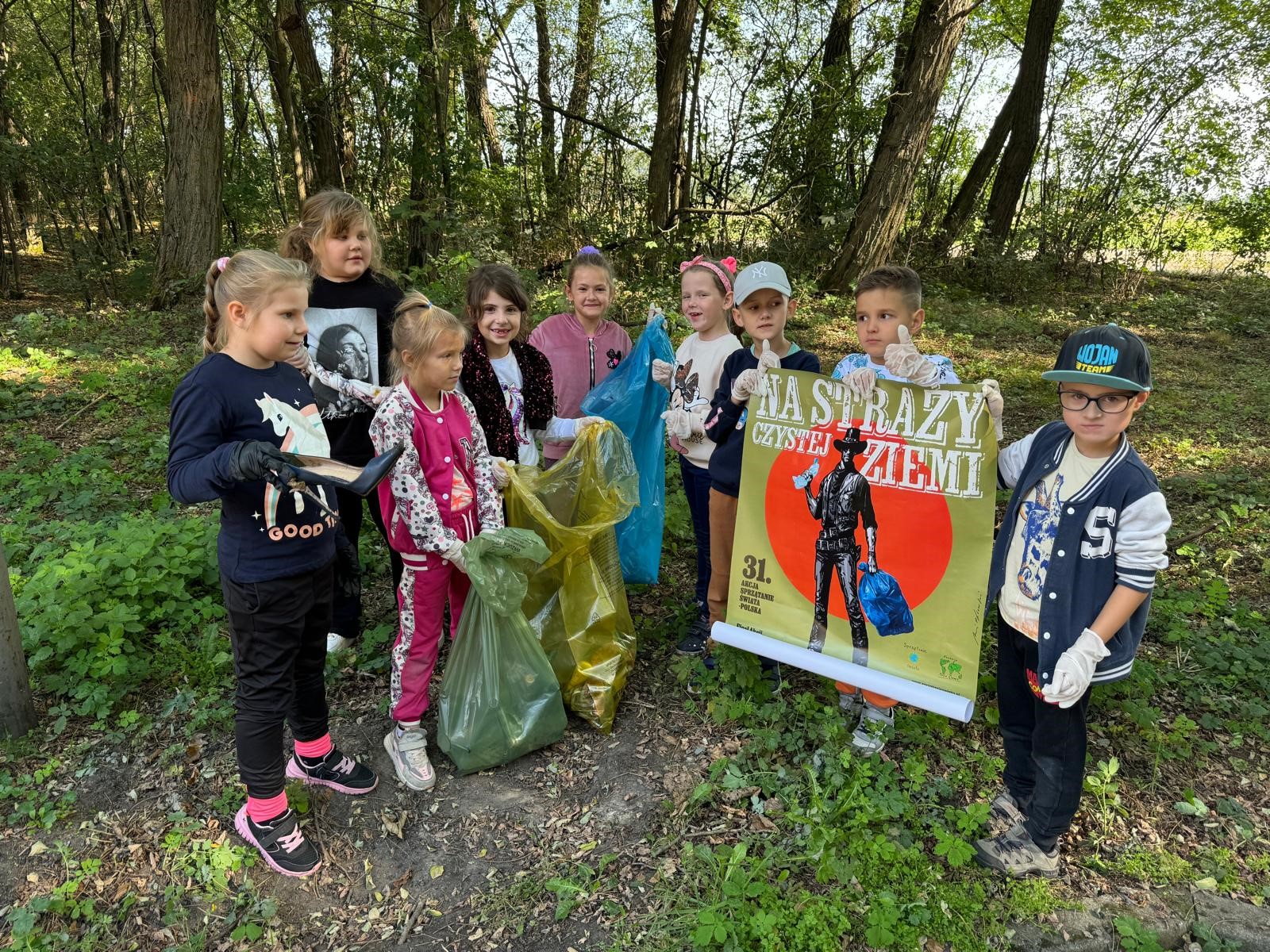 Dzieci stoją, trzymają plakat i worki w rękach