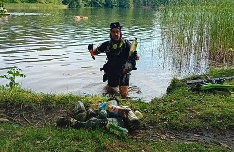 Nurek wychodzi z wody na brzeg jeziora. w rękach trzyma butelki 