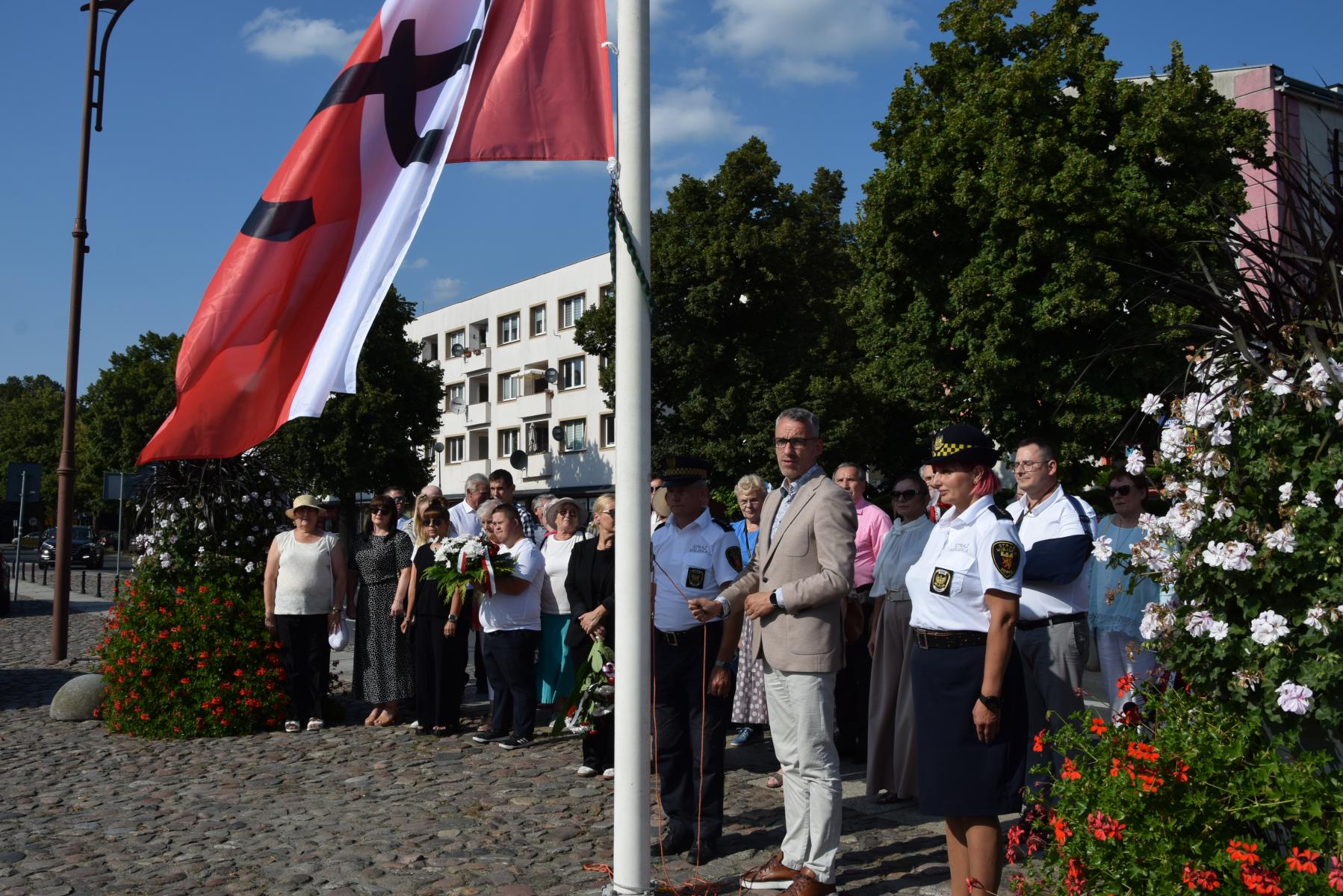 Burmistrz Dębna, w asyście strazników miejskich wciąga flagę na maszt 