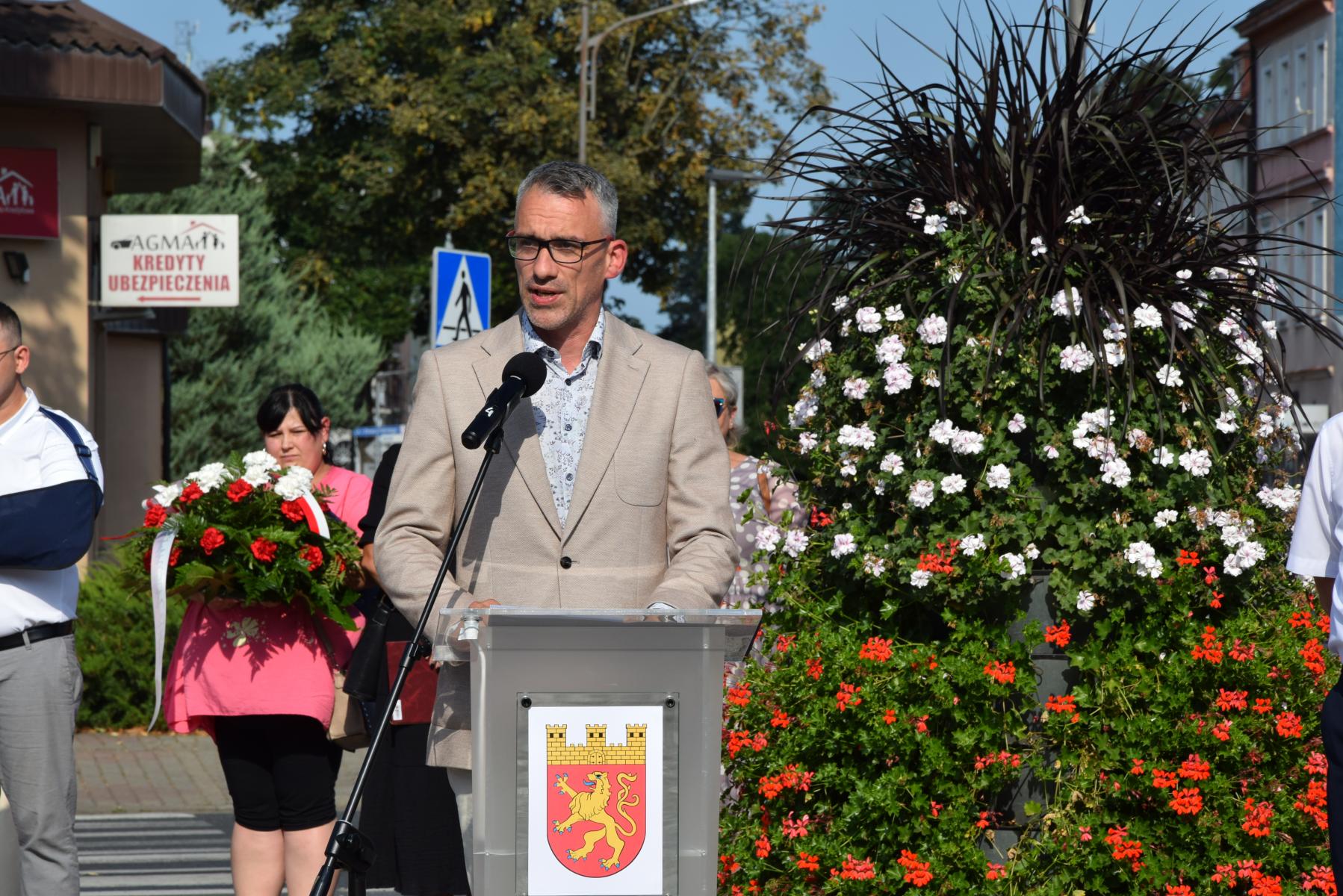 Burmistrz Dębna stoi przy mównicy, z tyłu wieża kwiatowa 