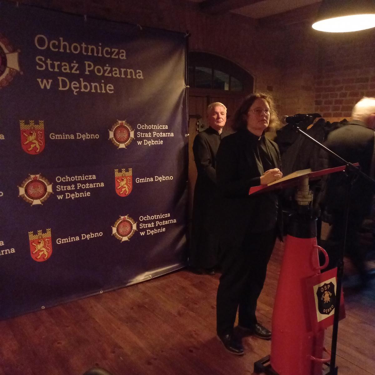 Pani pastor stoi przy mównicy, z tyłu stoi ksiądz w sułtannie