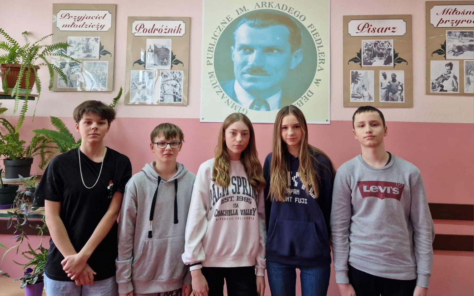 Pięcioro uczniów z SP2 Dębno, stoją w rzędzie, na holu, z tyłu zdjęcie patrona Arkadego Fiedlera 