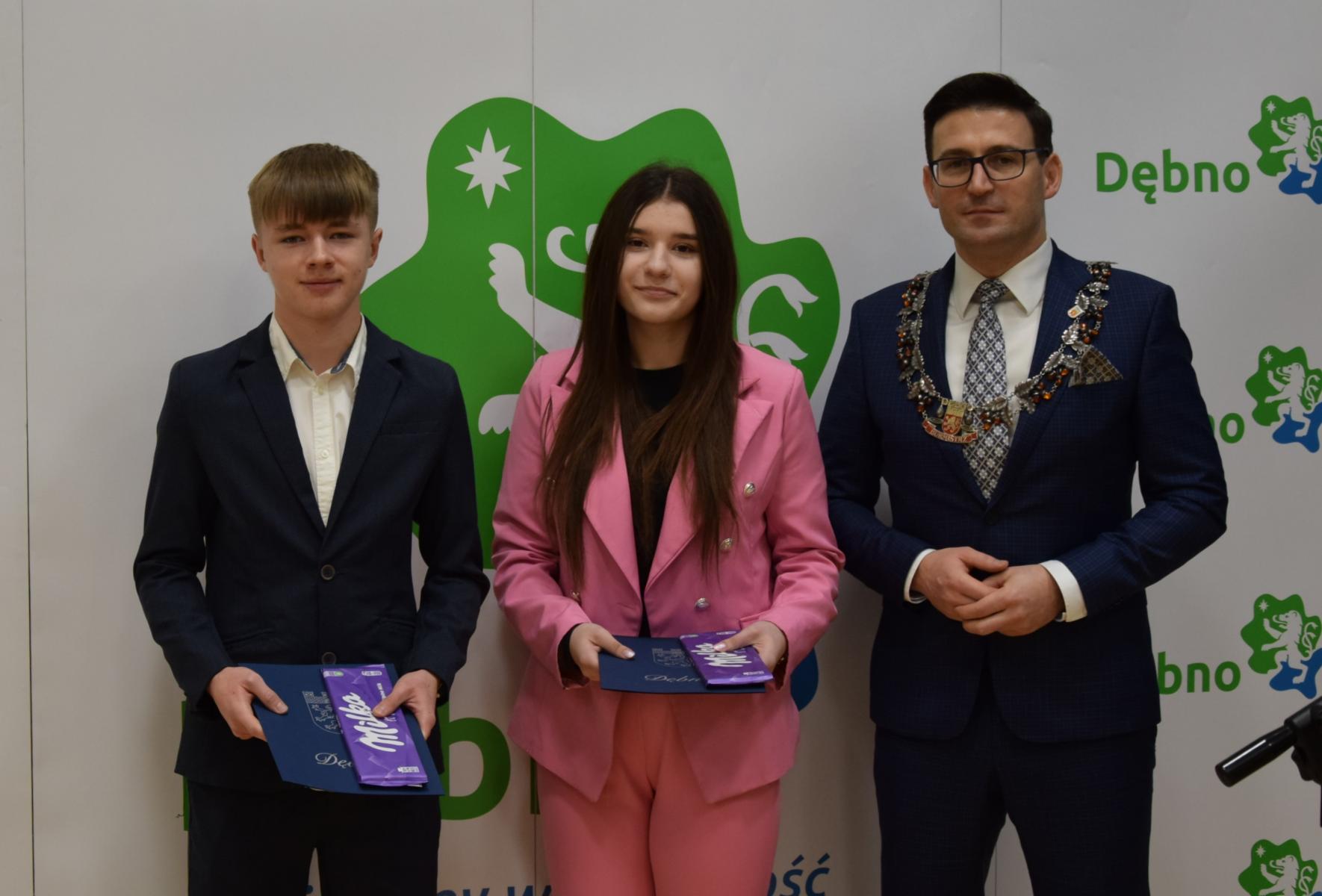 Od lewej stoją: Oliwier Pajor, Aleksandra Sala, Grzegorz Kulbicki. W tle biała ścianka, z logo zielono - niebieskim 