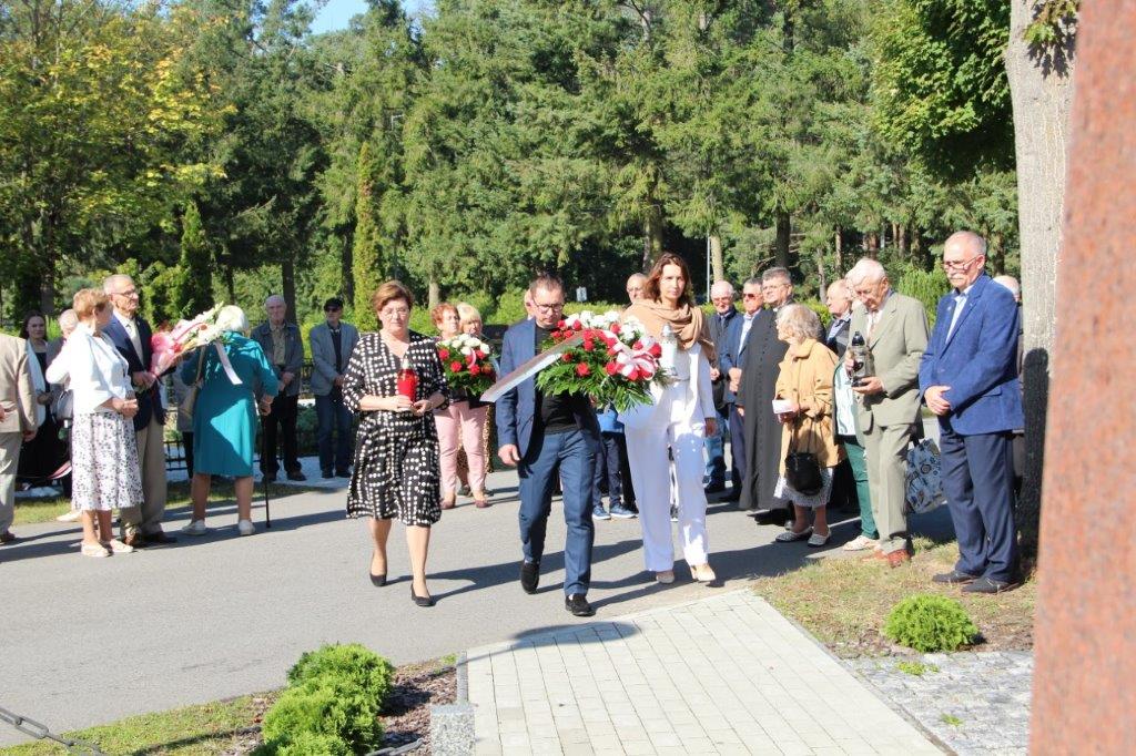Delegacja samorzadu składa kwiaty. Za nimi stoją ludzie 