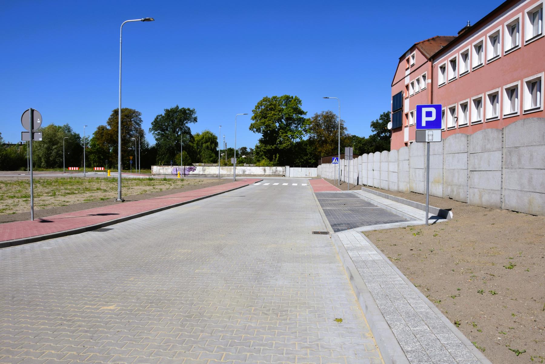 Droga z parkingami, po prawej widoczny budynek i betonowy płot