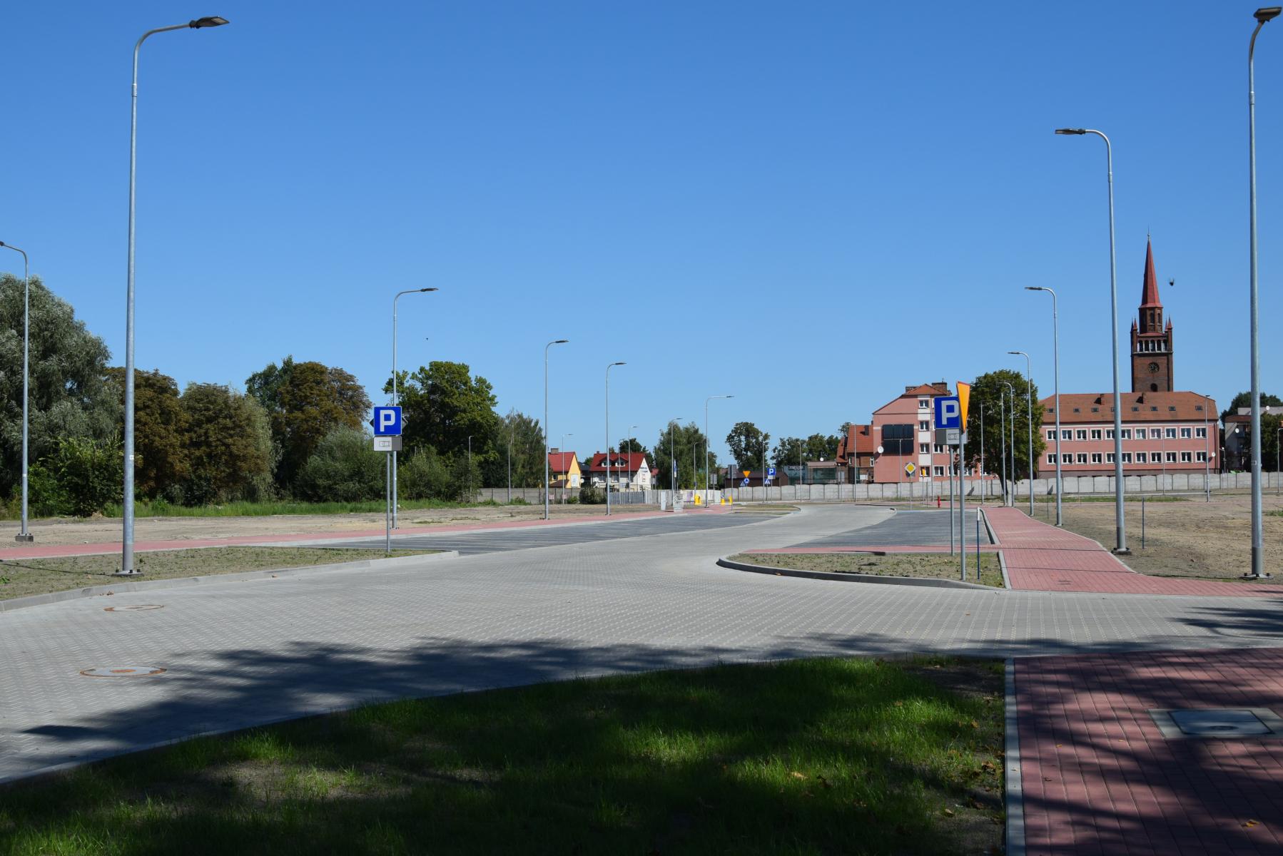 Układ dróg -Jezdnia z kostki szarej,, chodniki z czerownej kostki, miejsca parkingowe, lampy uliczne, niebeskie niebo 