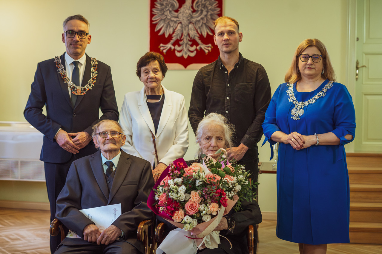 Para małeńska siedzi na krzełach, za nimi stoi burmistrz Dębna, kobieta, mężczyzna i kierownik USC