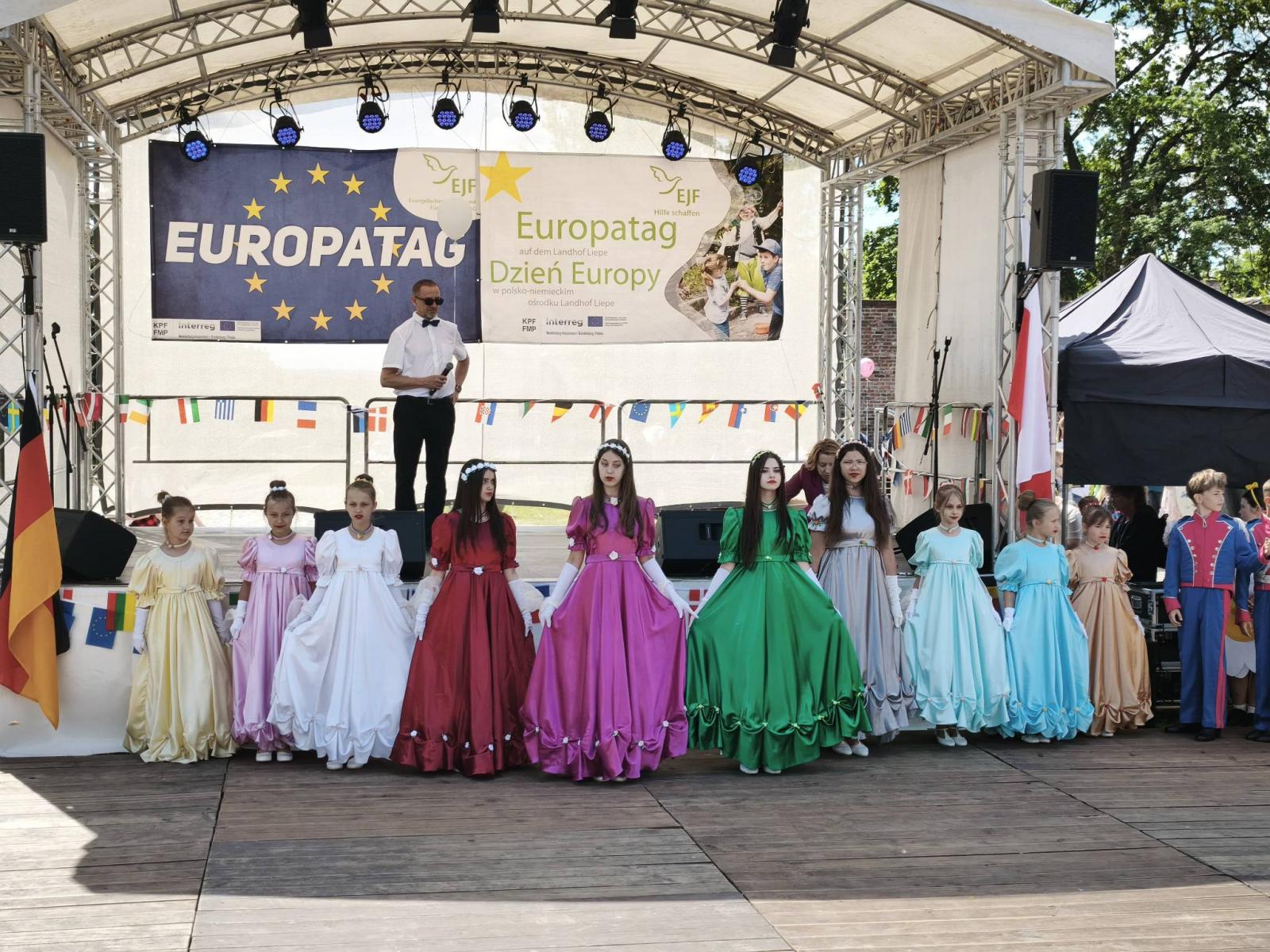 Zesp&oacute;ł Mali Cychrowiacy w kolorowych sukniach stoja na drewnianym parkiecie 
