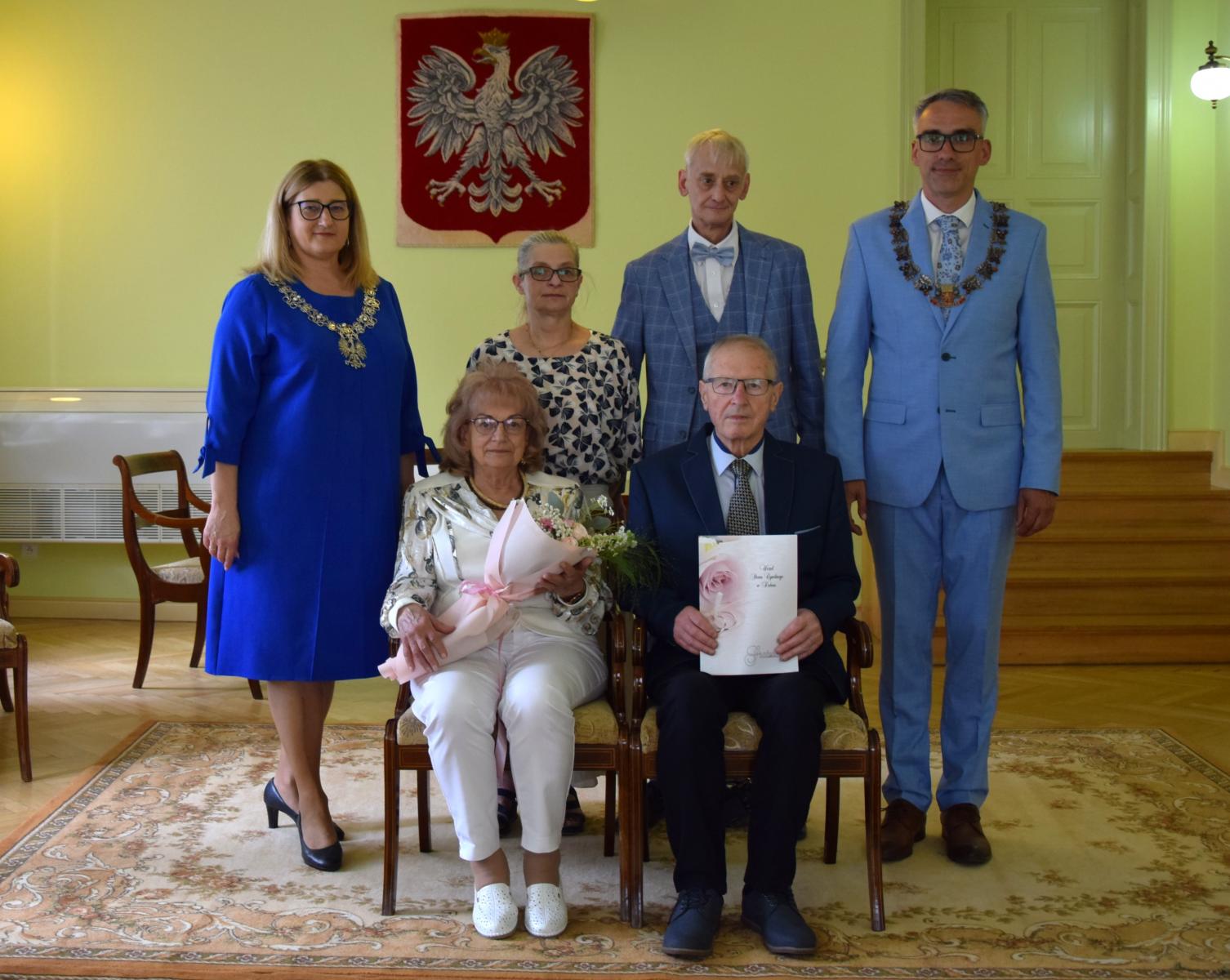 Jubilaci Państwo Obremscy siedzą na krzesłach w sali, za nimi stoi rodzina, pani kierownik z USC i Burmistrz Dębna