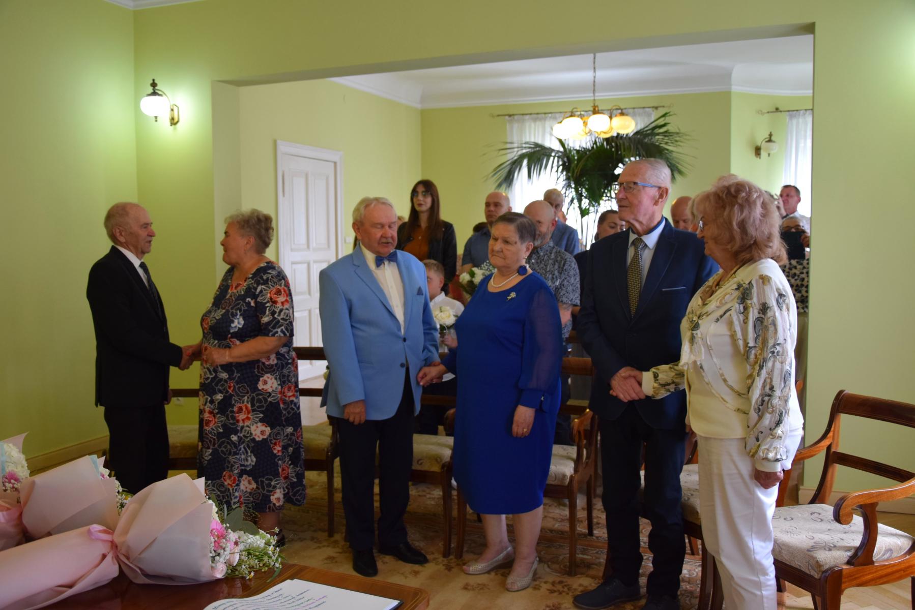 Pary małżeńskie stoją w sali, trzymają się za ręce