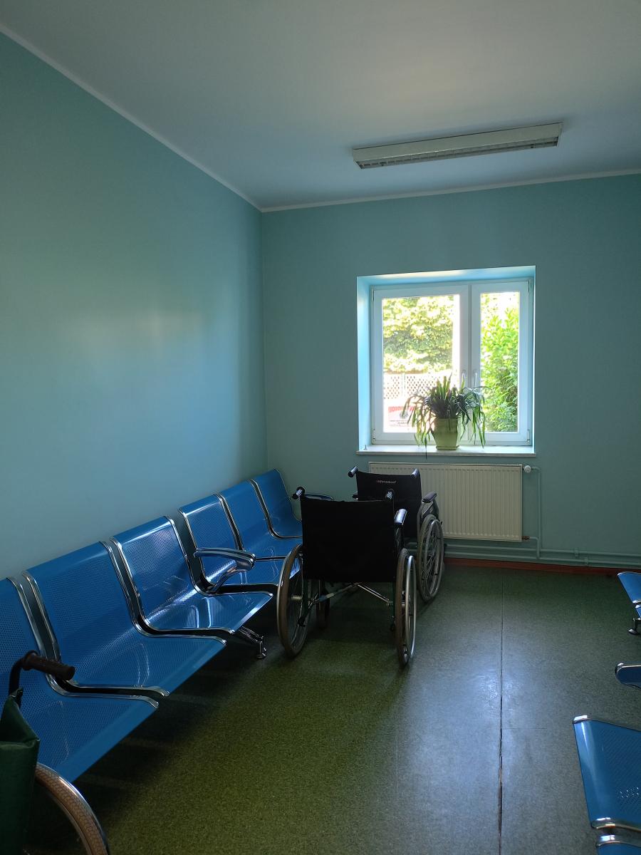 Pokój pomalowany na zielono, niebieskie krzesełka pod ścianą w rzędzie, dwa wózki inwalidzkie