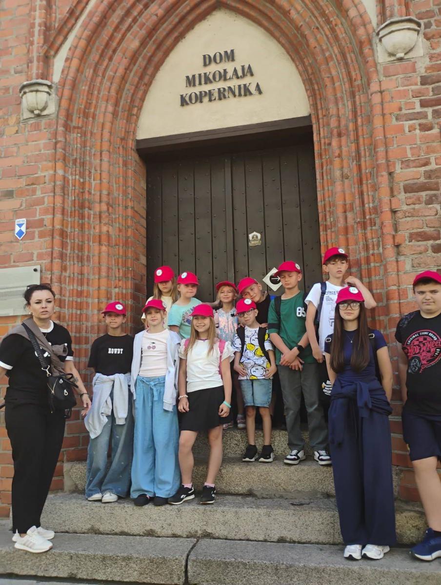Dzieci stoją przed budynkiem nad drzwiami napis Dom Mikołaja Kopernika