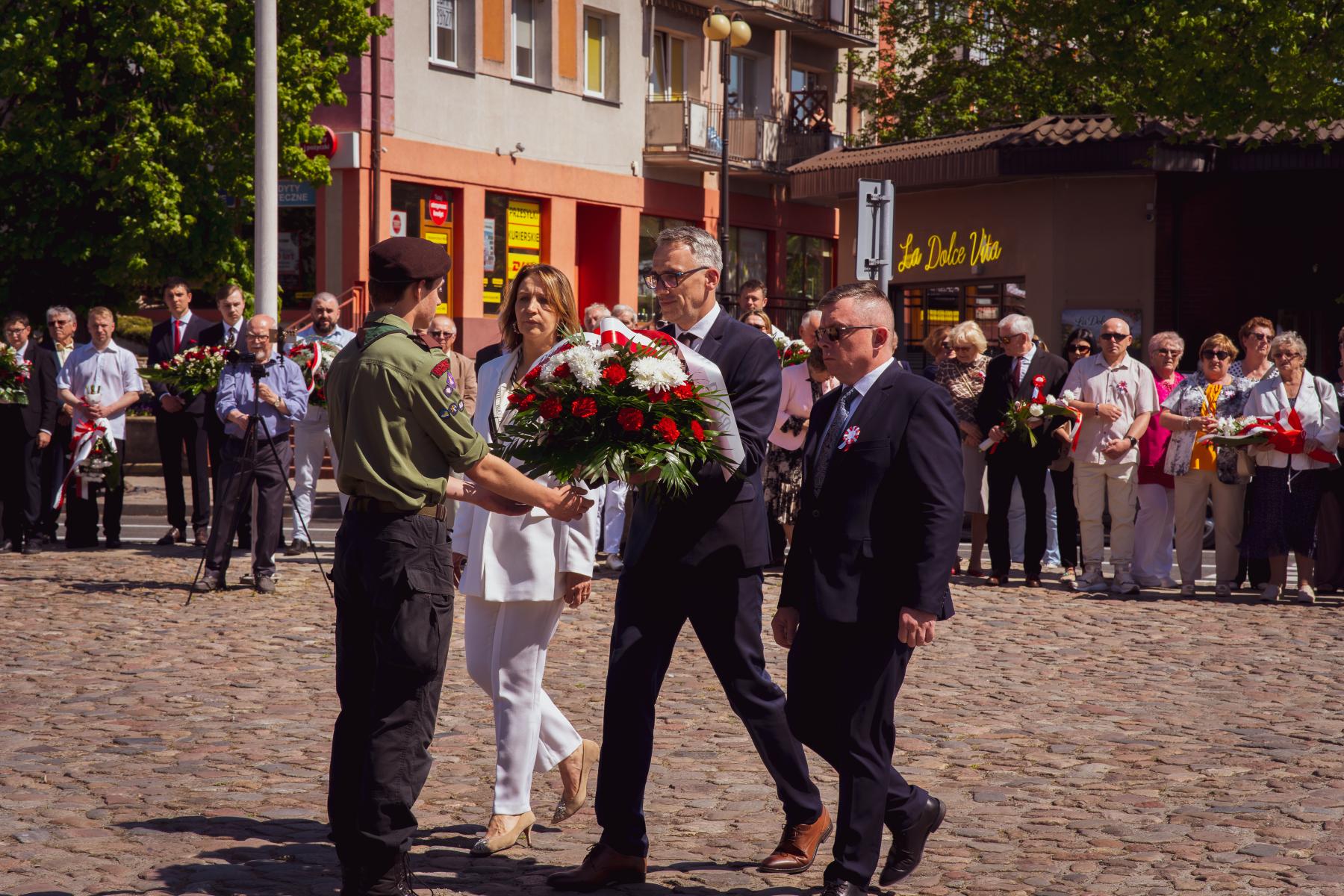 Delegacja samorządu (od lewej: pani zastępca, pan burmistrz, pan przewodniczący, przekazują wiązankę dla harcerza