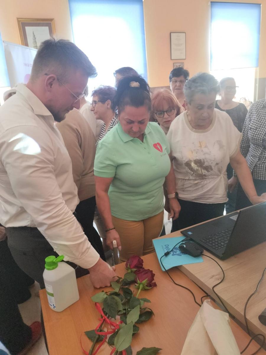 Mężczyzna stoi przy komputerze, kobieta trzyma urządzenie 