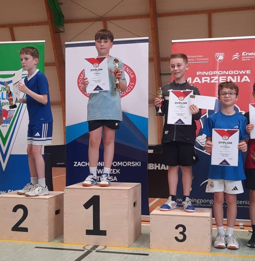 Antoni Kruszak stoi na najwyzszym podium, trzyma dyplom i puchar w ręku. 