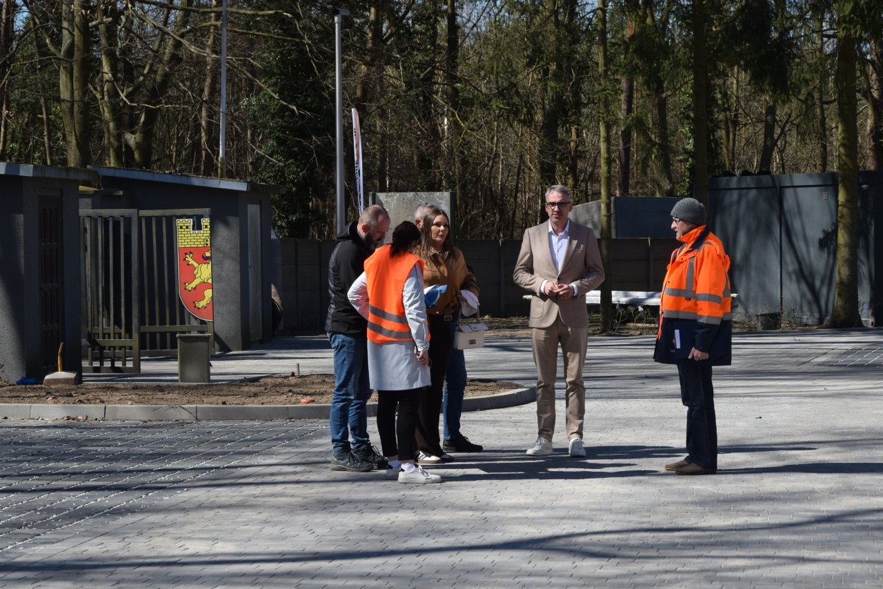 Grupa ludzi (w treści informajci wymienieni osobowo) stoi na placu podczas odbioru