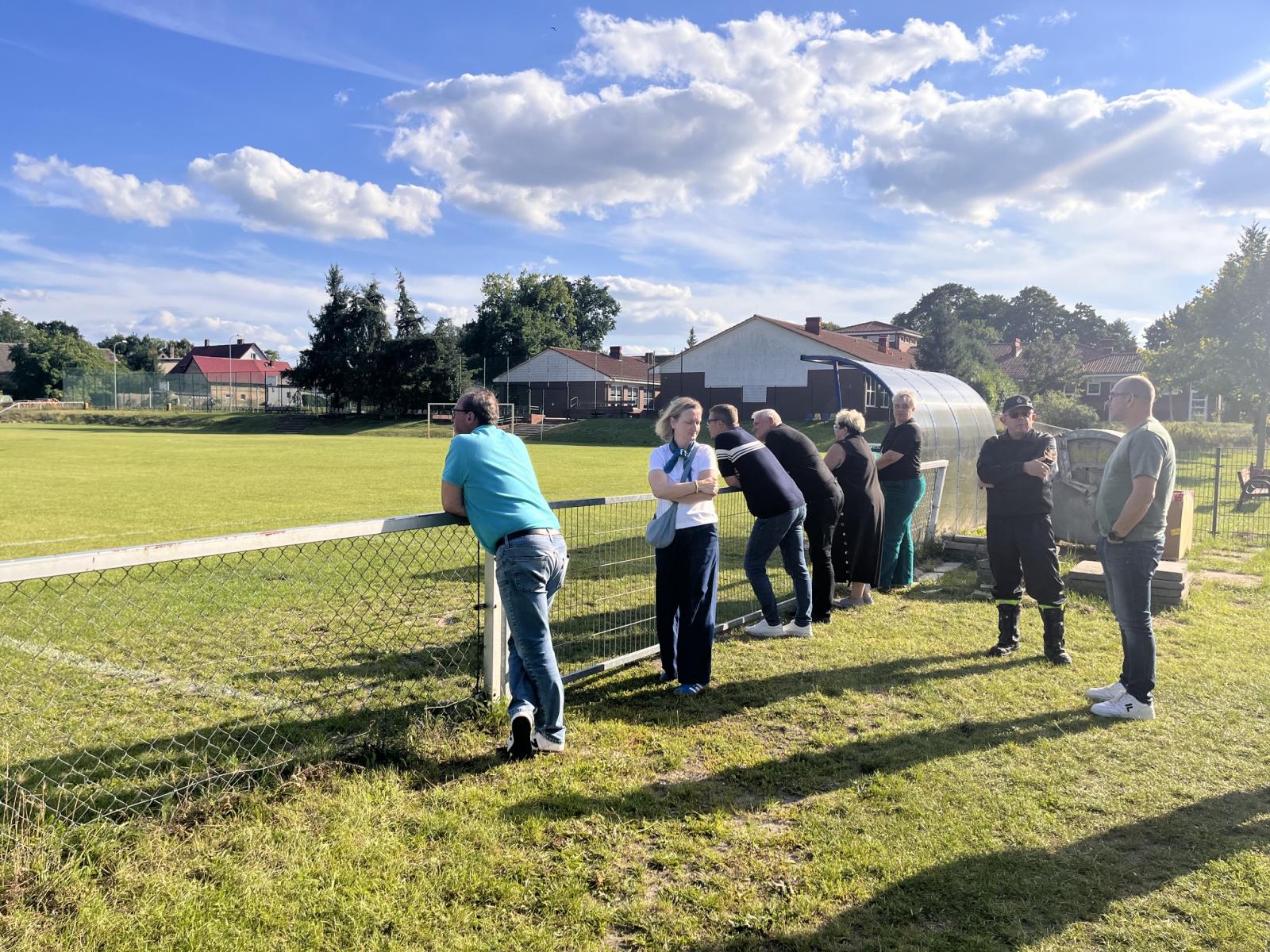 Członkowie komisji stoją przed zielonym boiskiem trawiastym 