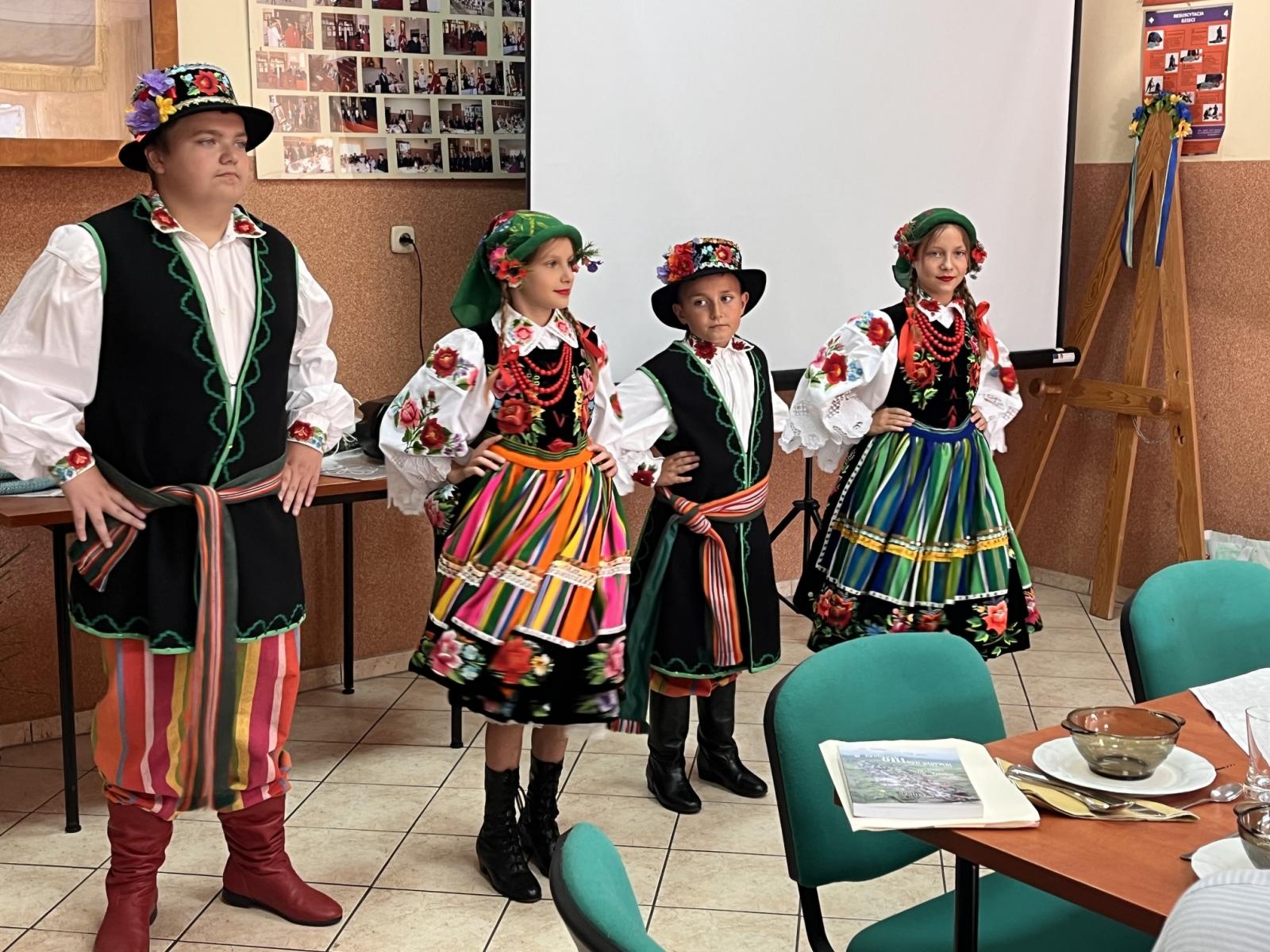 Czworto dzieci , na przemiennie chłopiec, dziewczynka ubrane w stroje łowickie, tańczą w sali