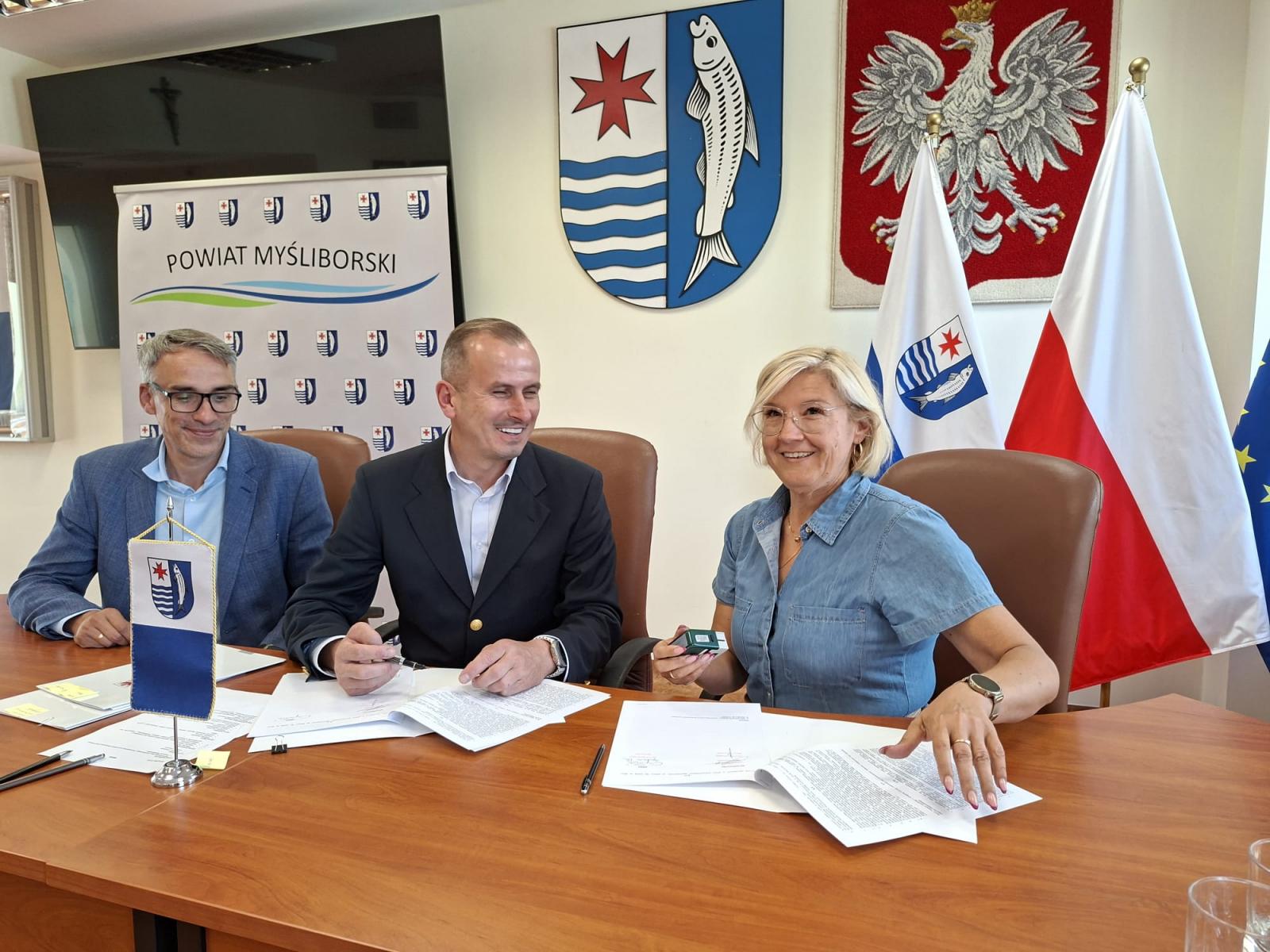 W sali posiedzeń siedzą przy stole i podpisują umowę od lewej: burmistrz Dębna, członek zarządu, pani sołtys