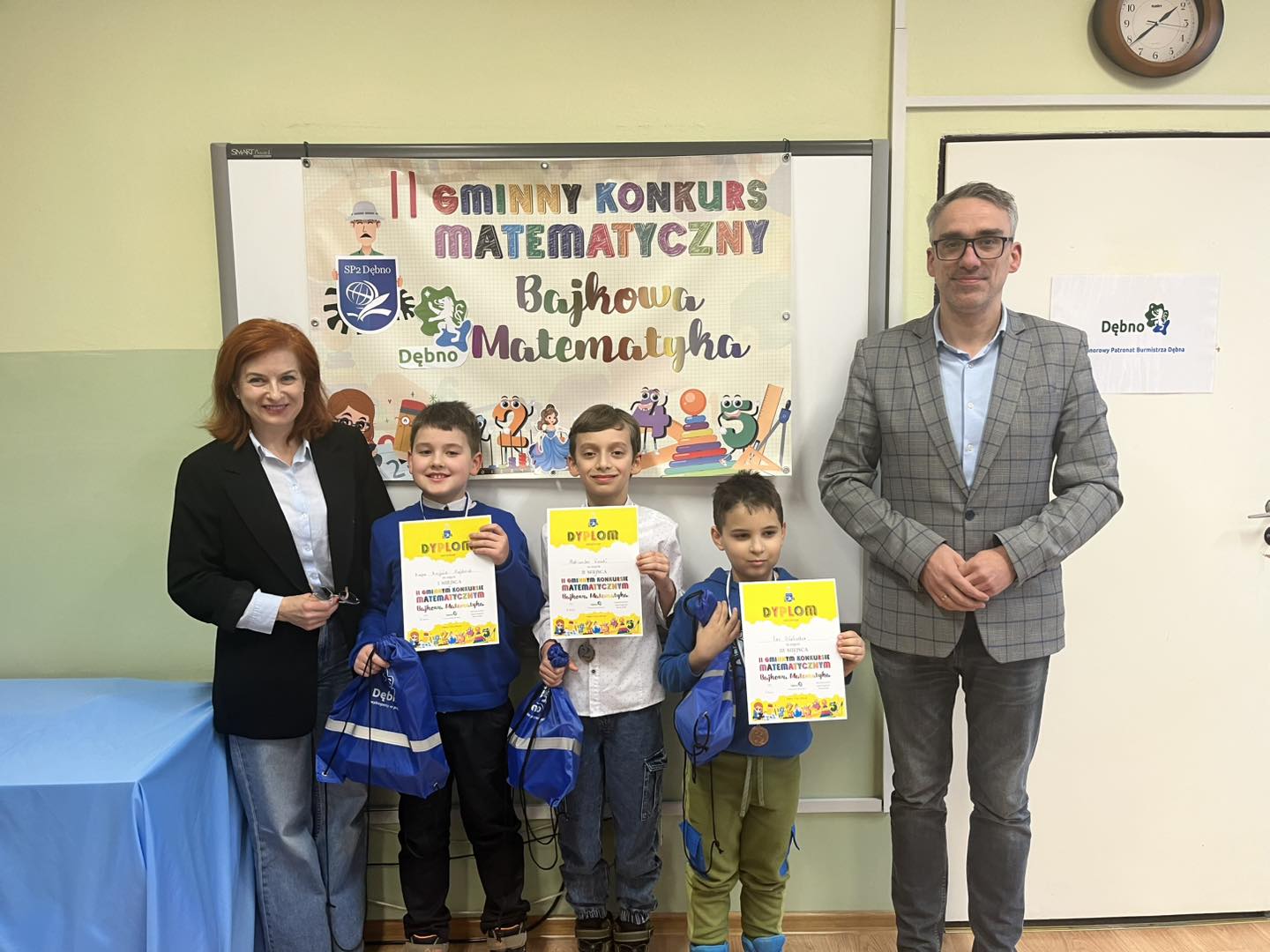 Od lewej, w klasie stoją: pani dyrektor, trzech chłopc&oacute;w z dyplomami w rękach, burmistrz