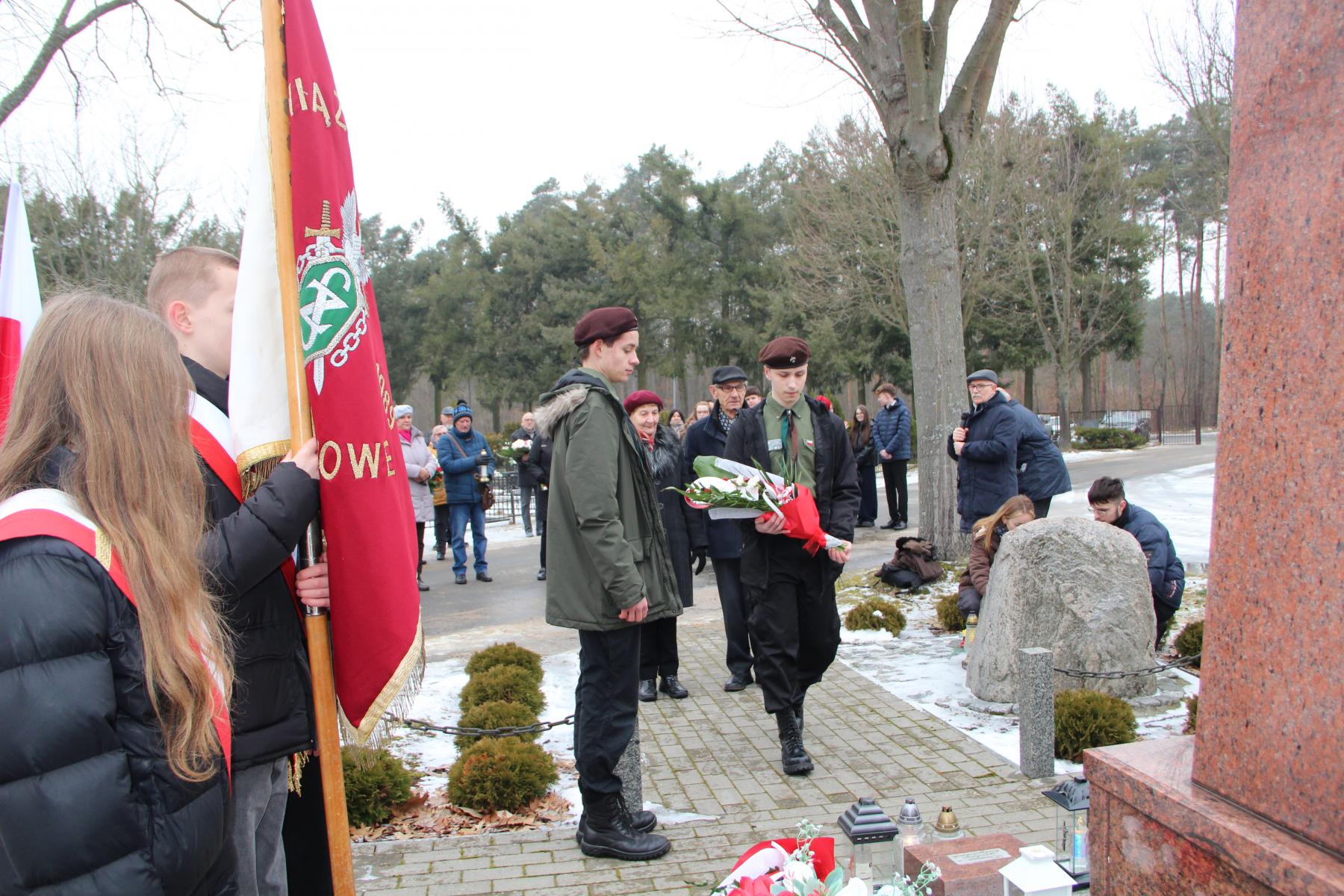 Na cmntarzu, Harcerze składają kwiaty przed pomnikiem, po lewej stoi poczet sztandawory, w tle ludzie 