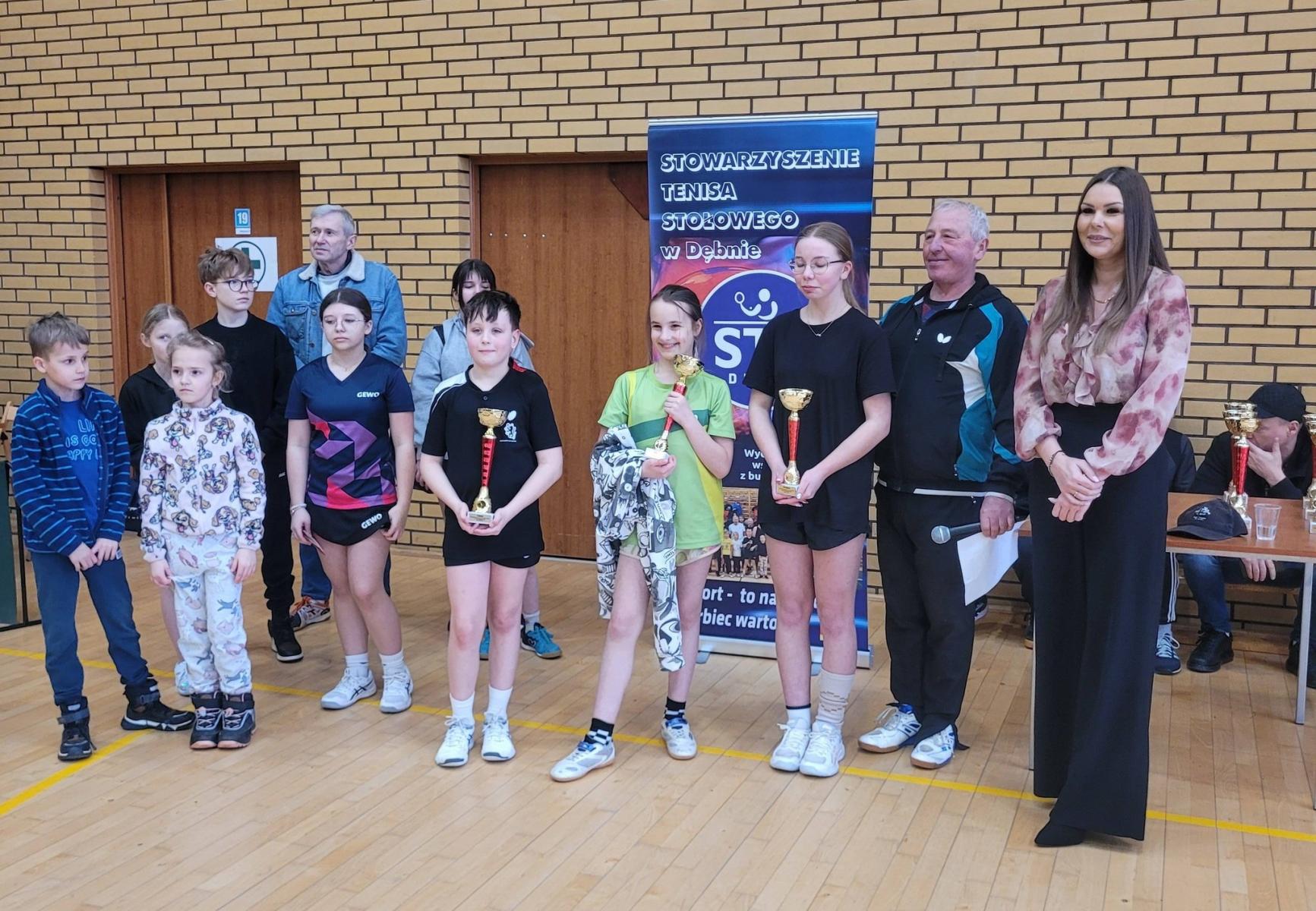 tr&oacute;jka dzieci po środku stoi z pucharami, po lewej obok stoi mężczyzna i kobieta