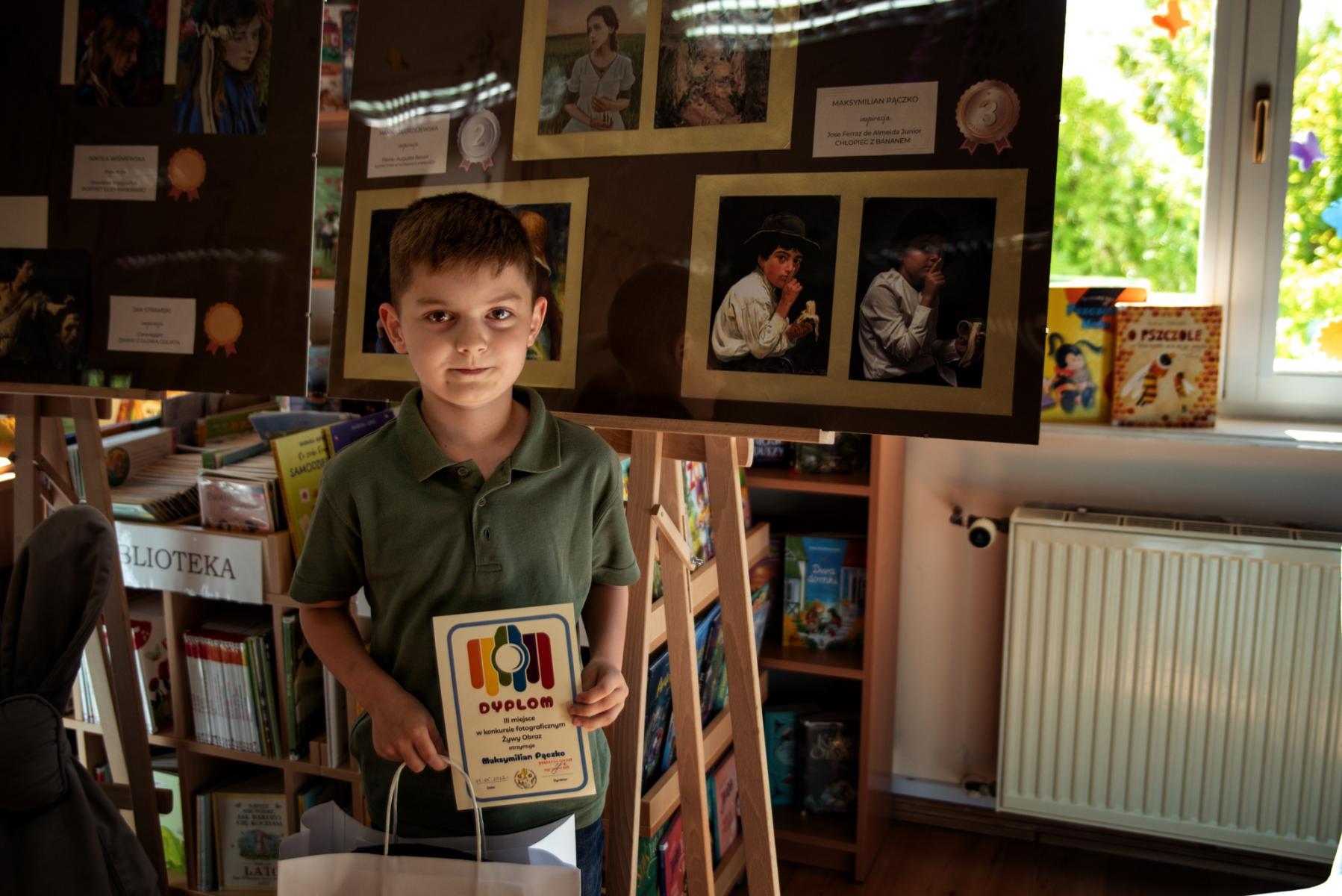 Maksymilian Pączko stoi z dyplomem, w tle jego praca
