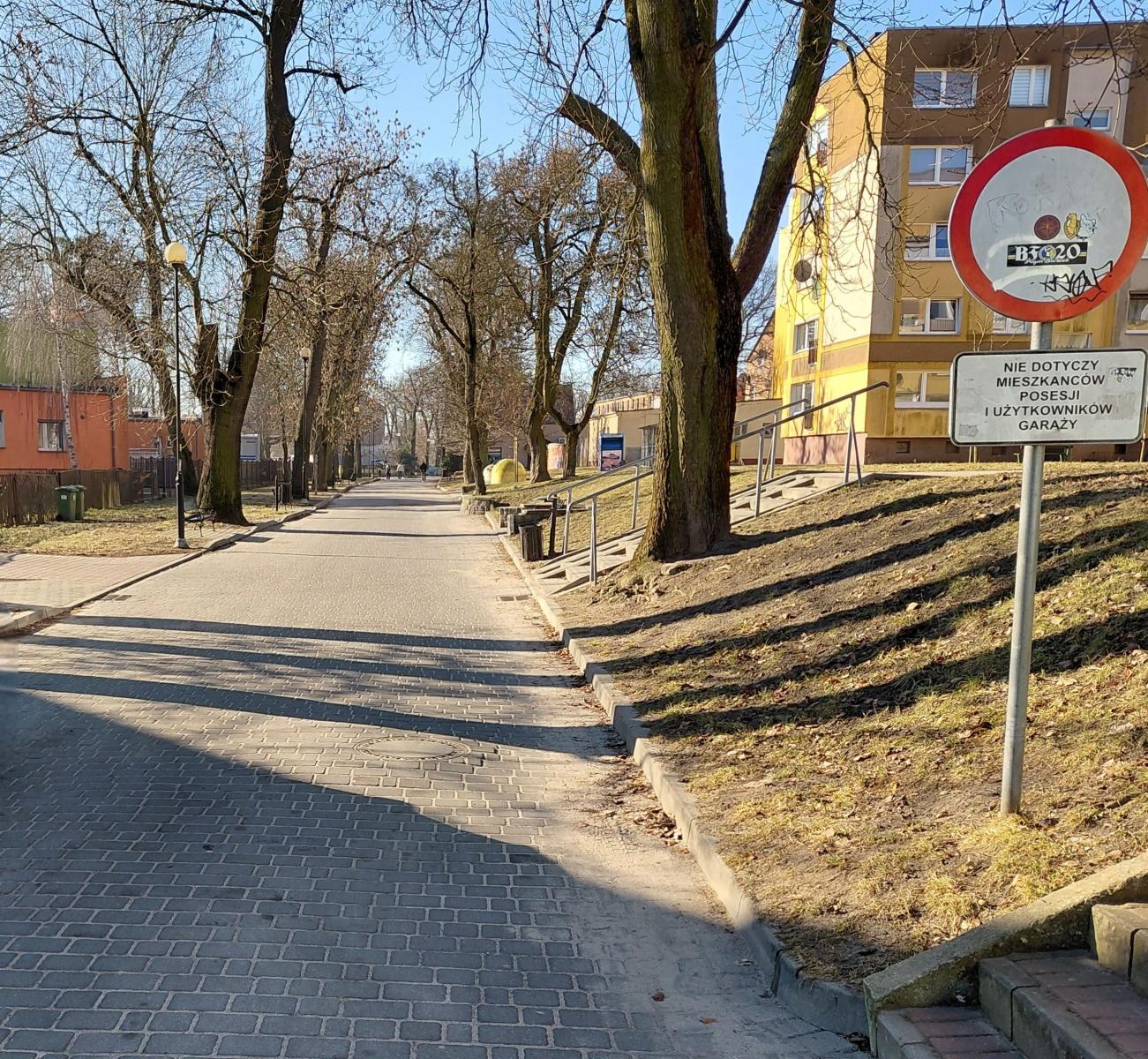 Szeroka droga dla pieszych , ze znakiem, po bokach drzewa 