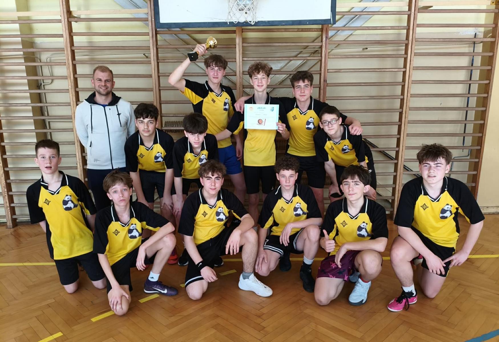 Zwycięska drużyna chłopców wraz z opiekunem na sali, w tle drewniane drabinki