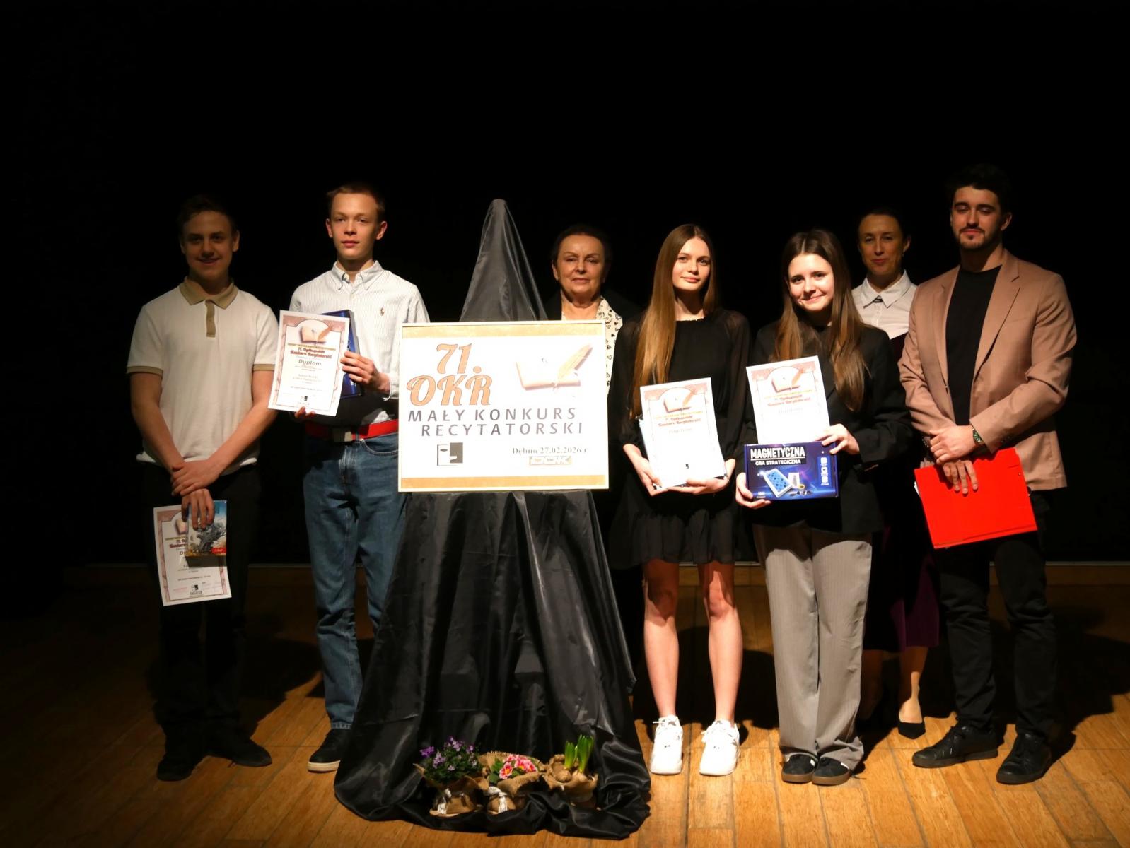 Wyr&oacute;znieni uczniwoie w kategorii VII-VIII w sali, trzymają dyplomy w rękach, za nimi stoją członkowie jury