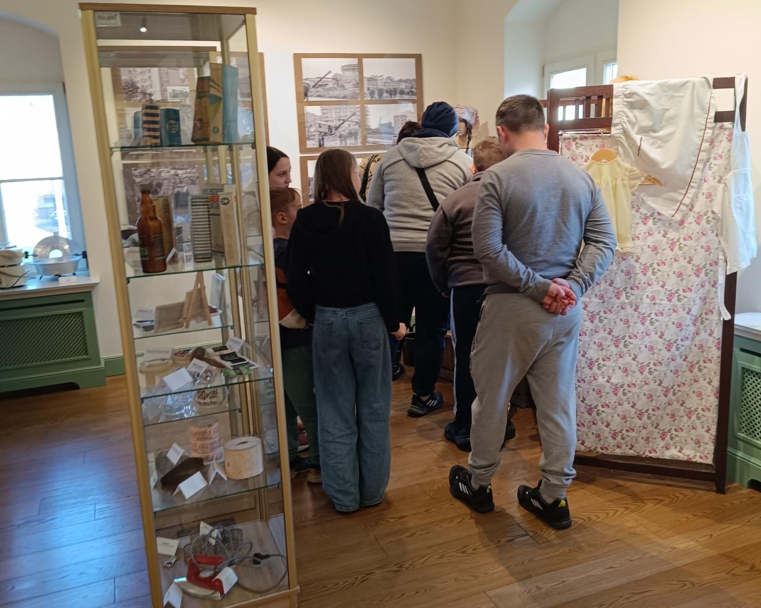 Sala ekspozycyjna, w niej ludzie ogladają eksponaty, na środku stoi gablota z przedmiotami 