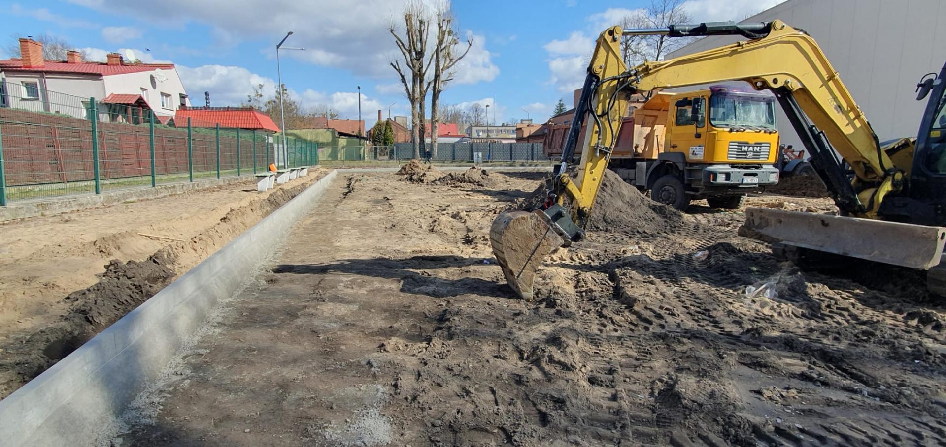 Koparka na placu budowy, z lewej strony ułożone krawężniki
