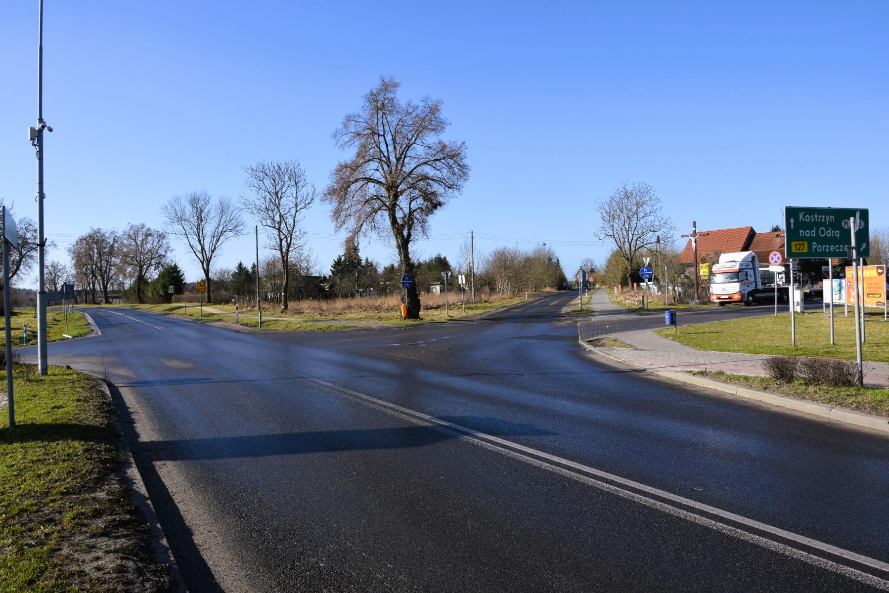 Skrzyżowanie dr&oacute;g , na poboczu drzewa, w tle dom