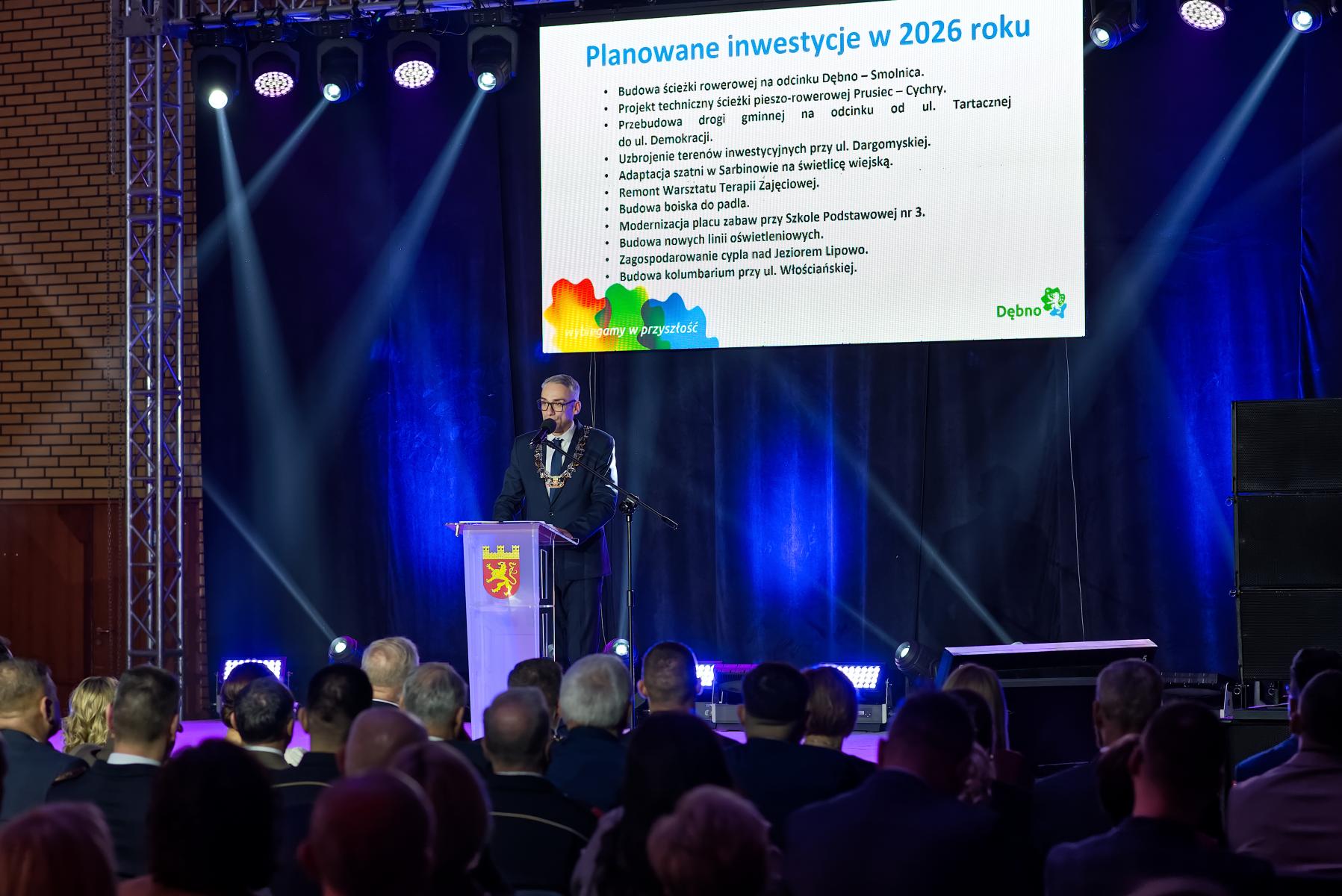 Burmistrz stoi na scenie przy m&oacute;wnicy, za nim prezentacja ze slajdem 