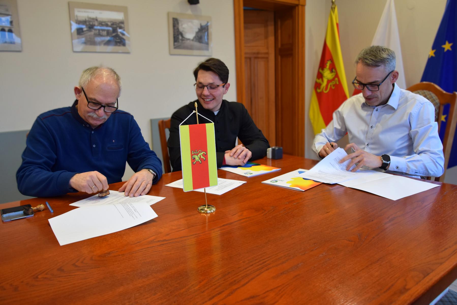 Trzech mężczyzn w sali siedzi przy stole 