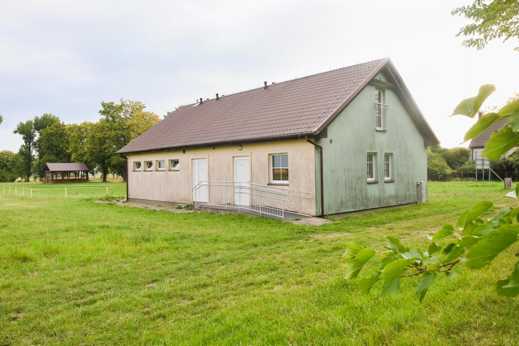 Budynek szatni od tyłu. w tle wiata drewniana, trawa, niebo, drzewa