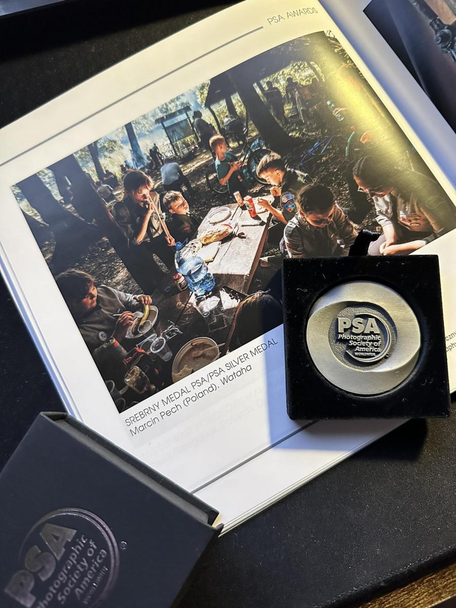 Album ze zdjęciem harcerzy z lesie , siedzą przy ławce, spożywają posiłek. na tym srebrnymedal 