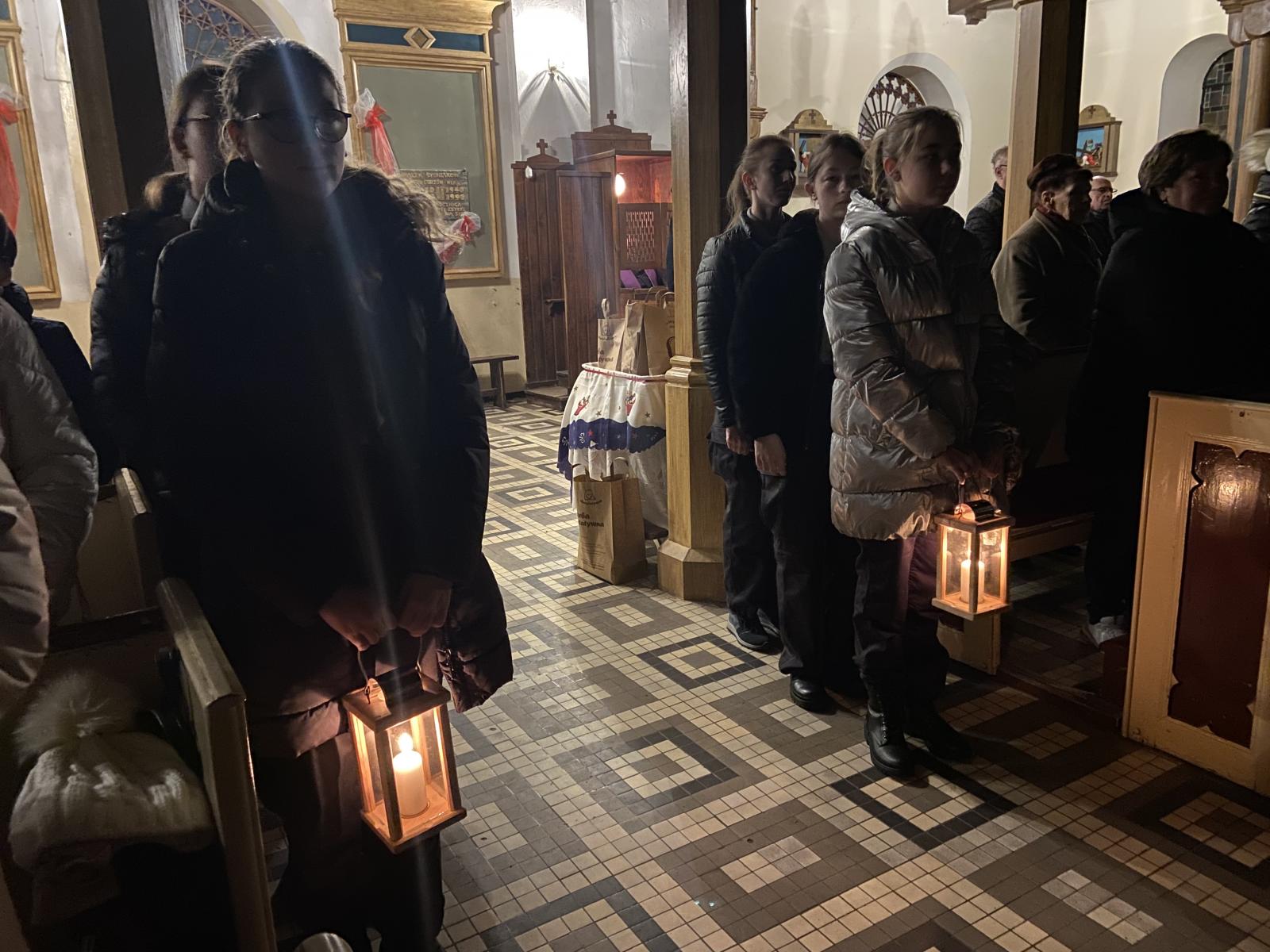 Harcerze stoją  w dwóch rzędach. Dwie z przodu harcerki trzymają lampiony ze światełkiem