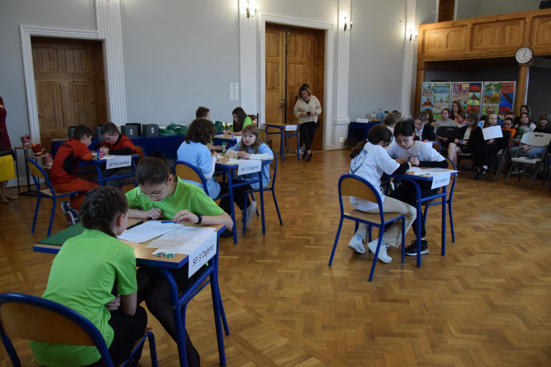 Drużyny siedzą przy stoilkach i rozwiązują zadania