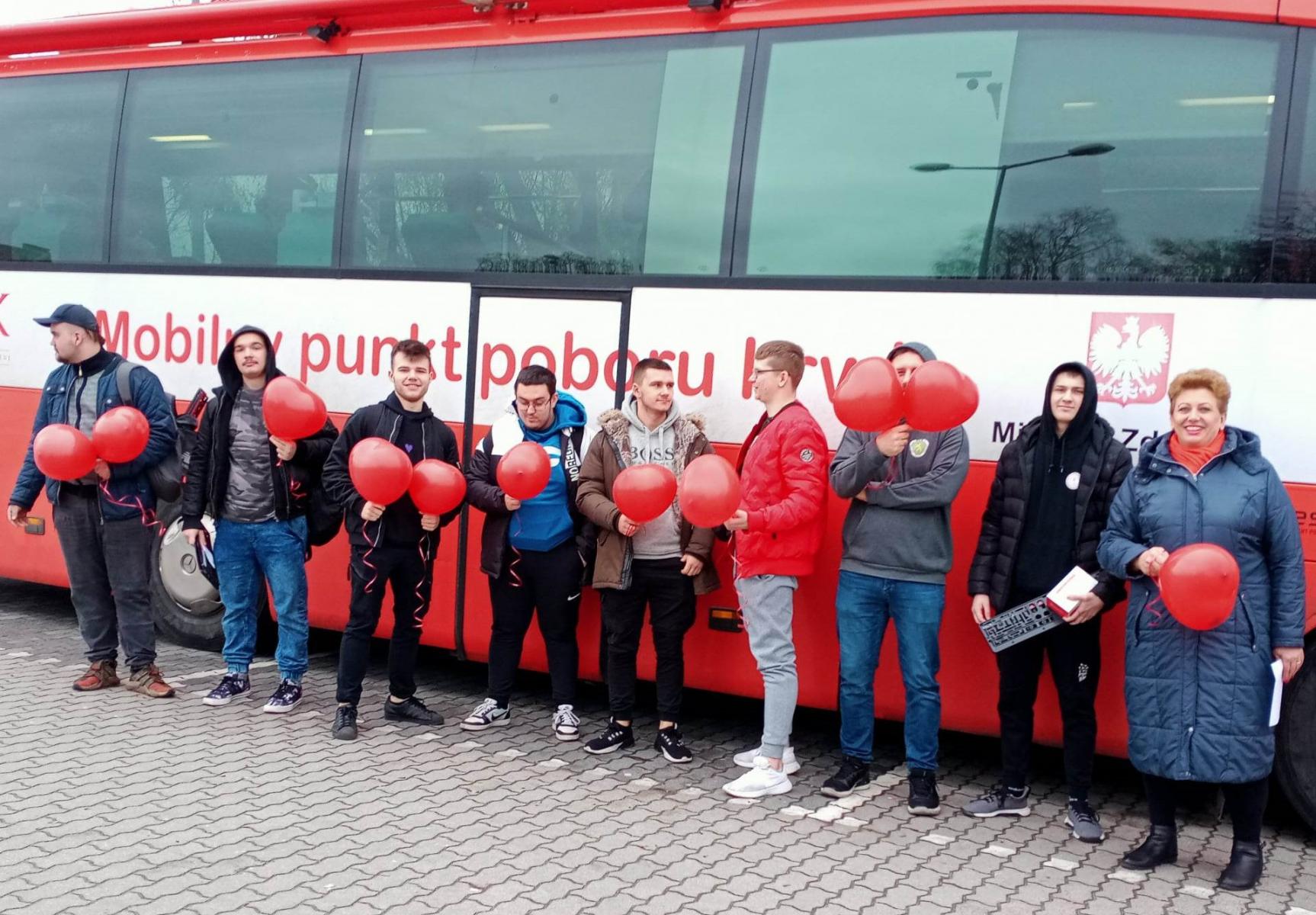 Uczniwoie stoją w rzędzie przed krwiobusem