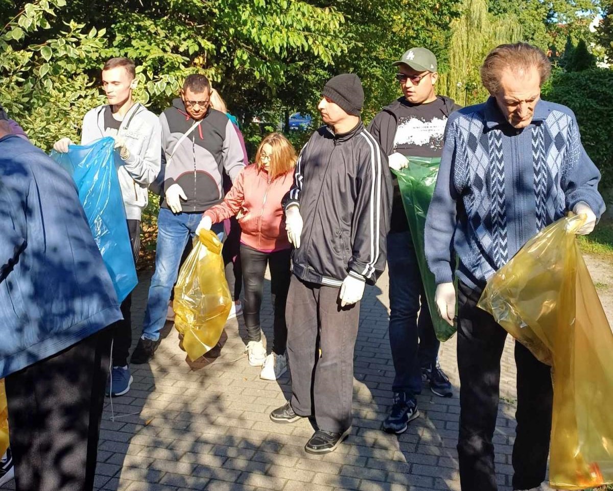 Grupa osób z workami idzie przez deptak. W tle drzewa
